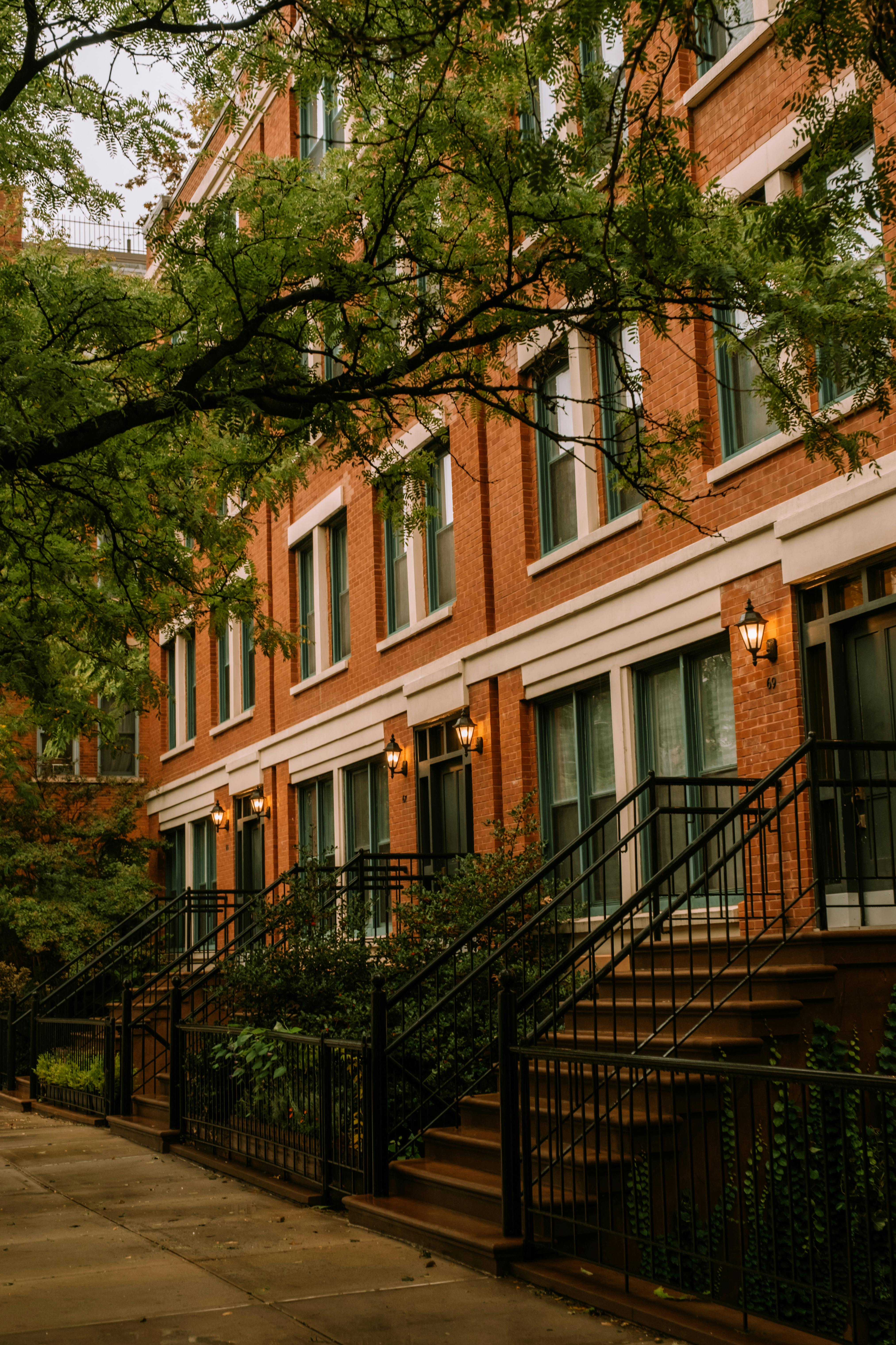 Elegant row of red brick townhouses with stairs and greenery on a city street.