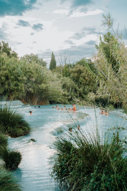 Adults enjoying a serene soak in natural hot springs surrounded by verdant greenery during daytime.
