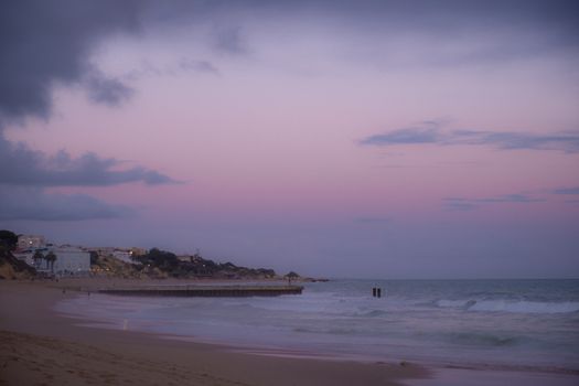 A serene beach scene with a pink sky and calm waves at sunset.