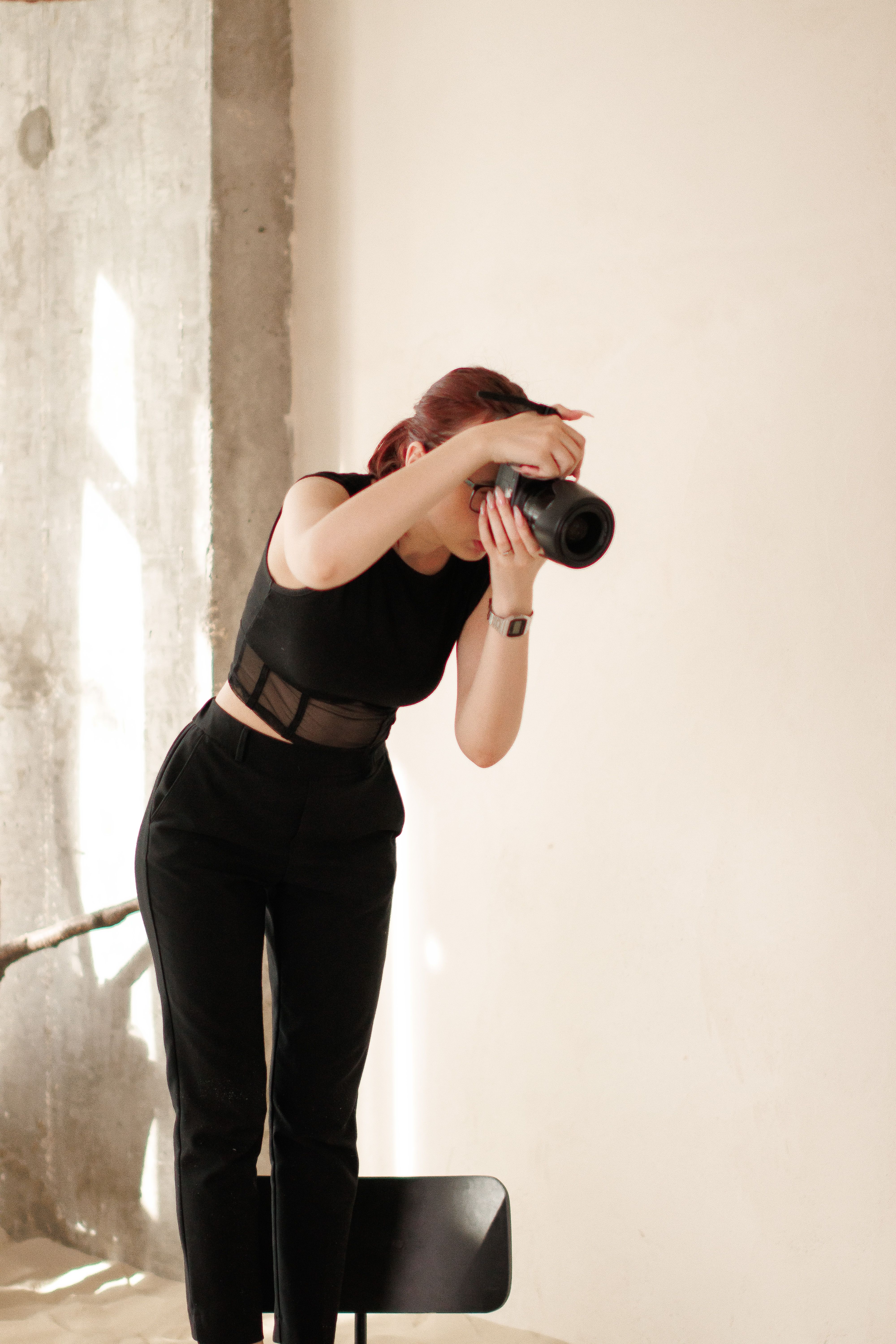 A woman in a black outfit photographs indoors with natural light.