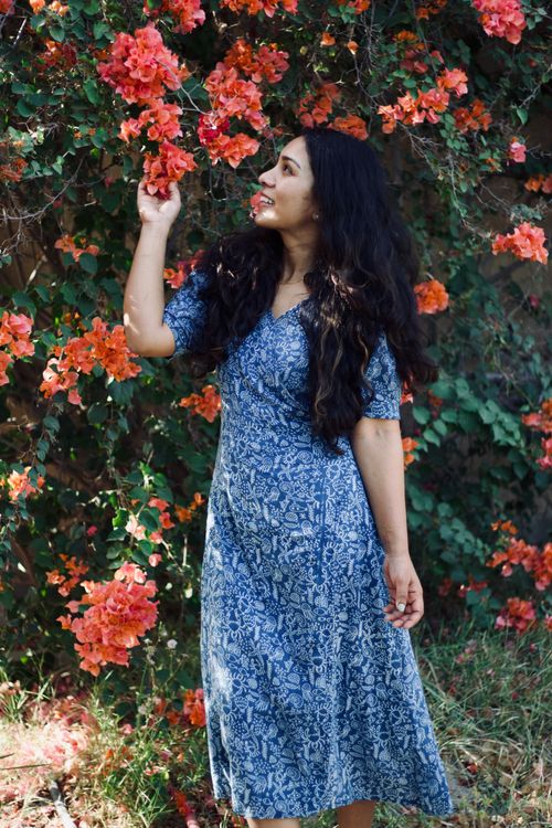 Free A joyful woman in a blue floral dress stands admiring vibrant flowers in a garden. Stock Photo
