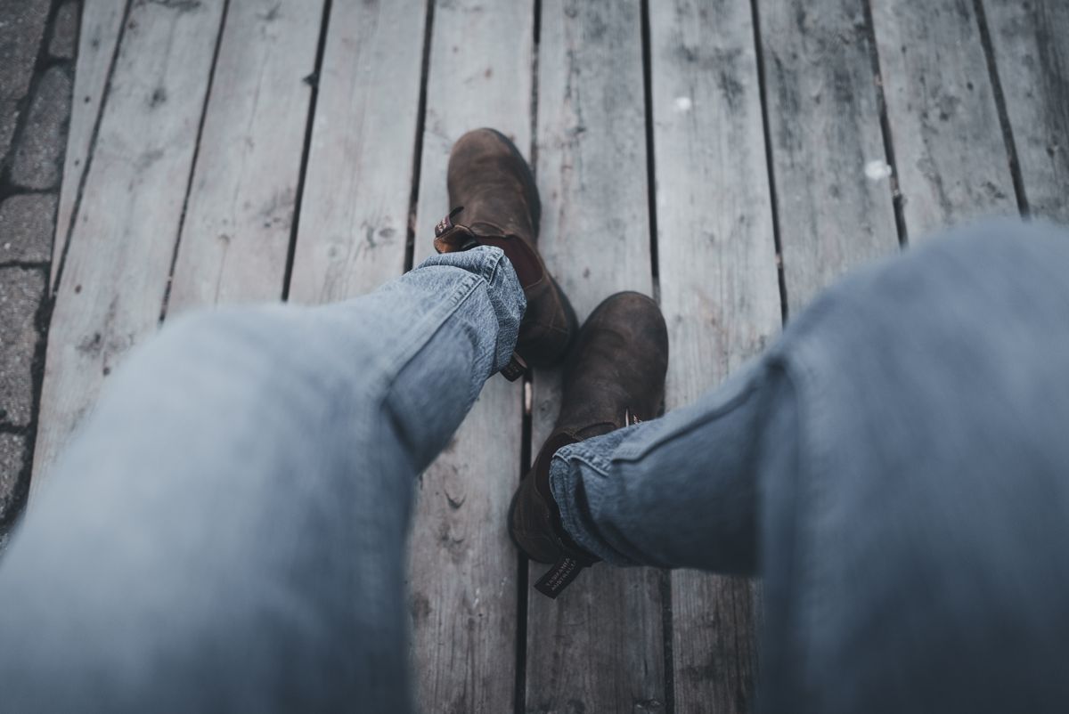 Casual outfit pairing jeans with brown ankle boots on a wooden floor