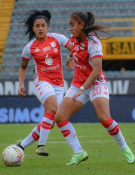 Two women playing soccer in a dynamic outdoor match on a grassy field.