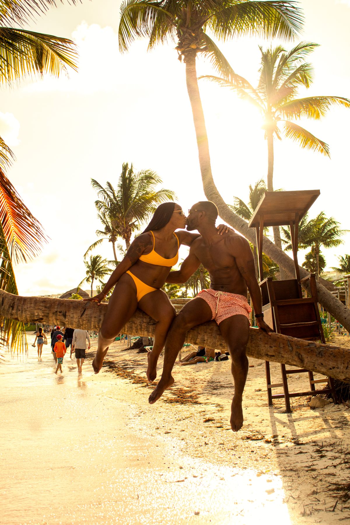 A couple enjoys a romantic kiss on a palm tree at sunset on Akumal Beach, Mexico.
