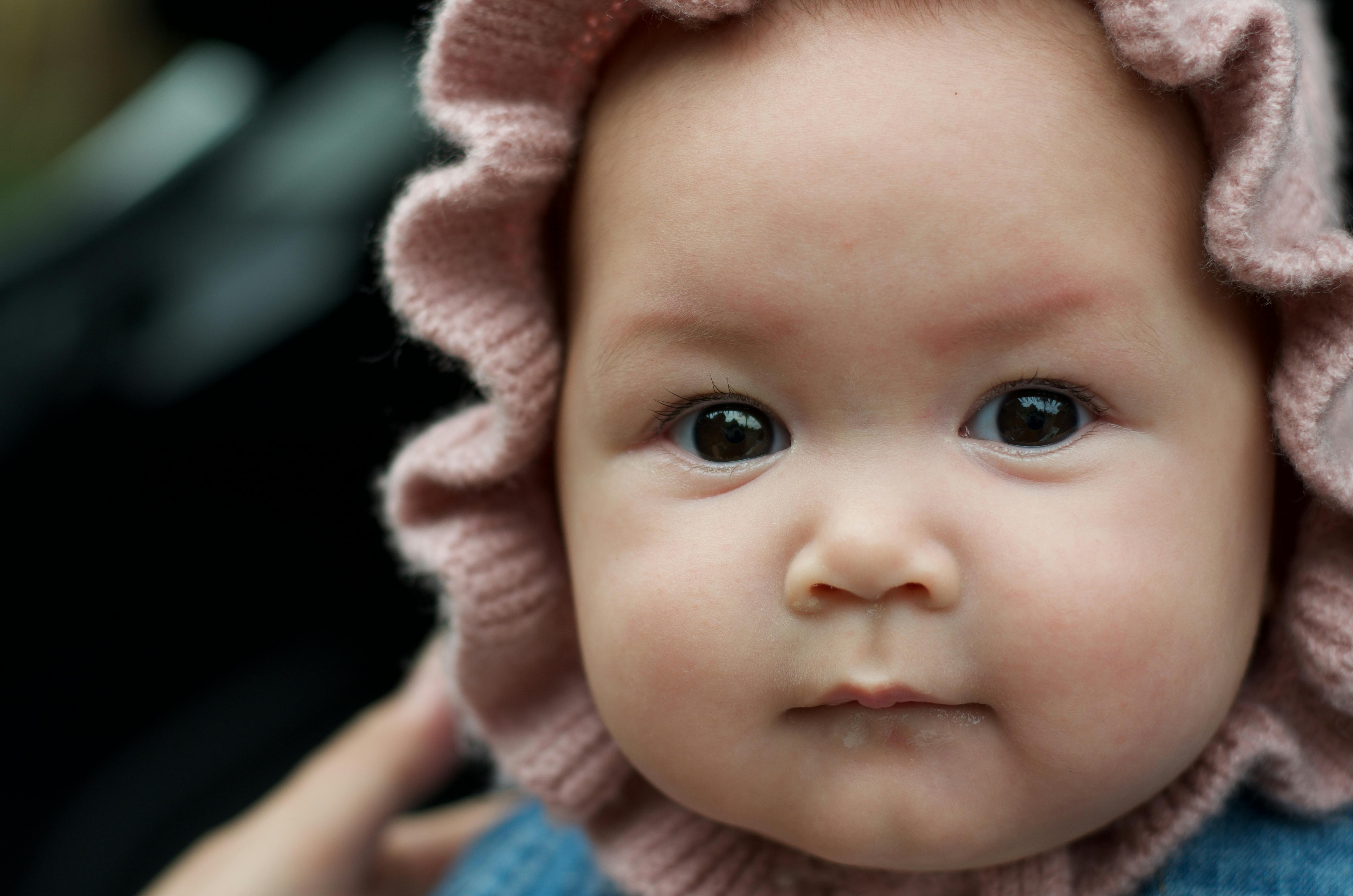 Charming close-up portrait of a baby wearing a pink hat, showcasing big eyes and soft features.