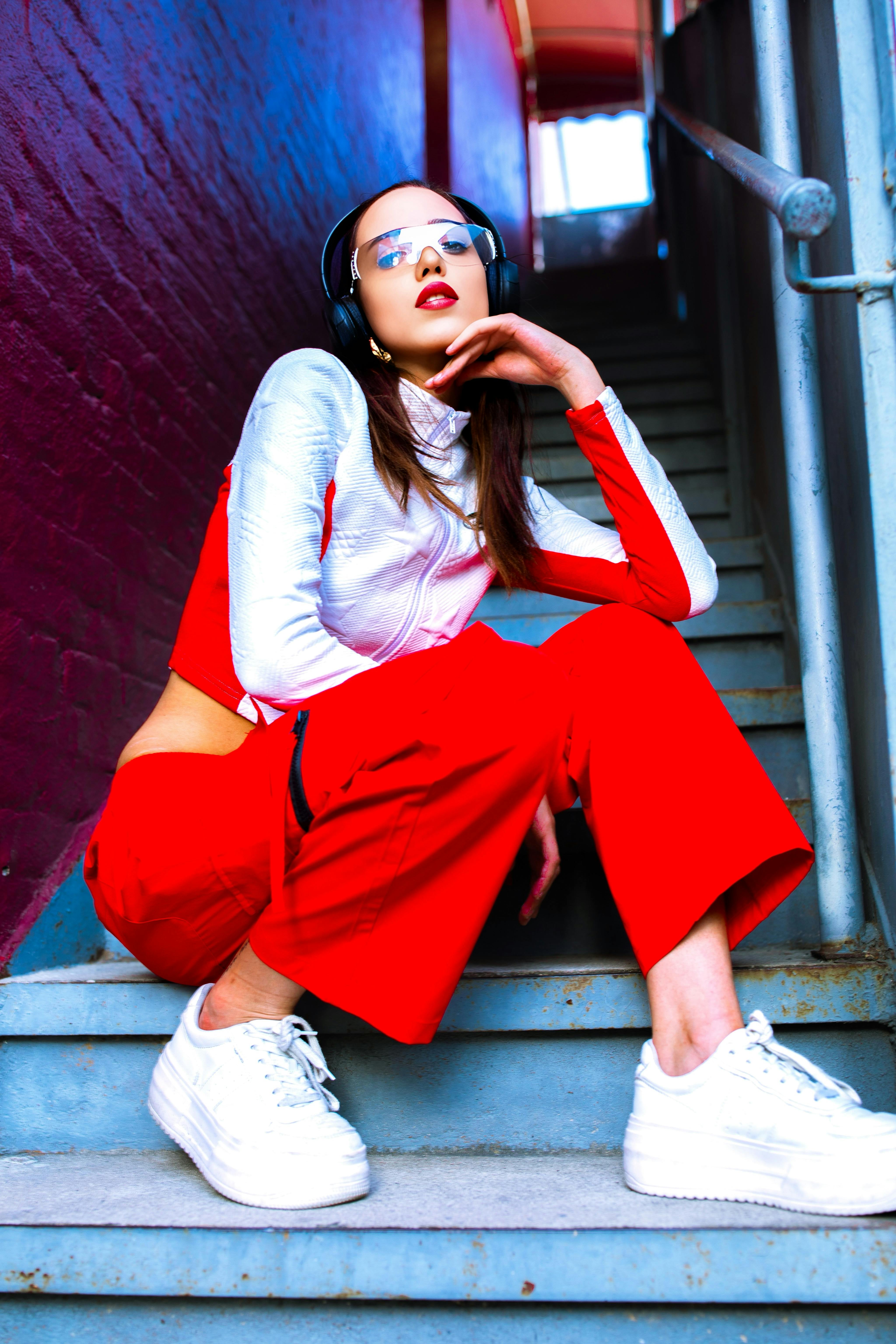 A stylish woman in edgy streetwear sitting confidently on stairs with headphones.
