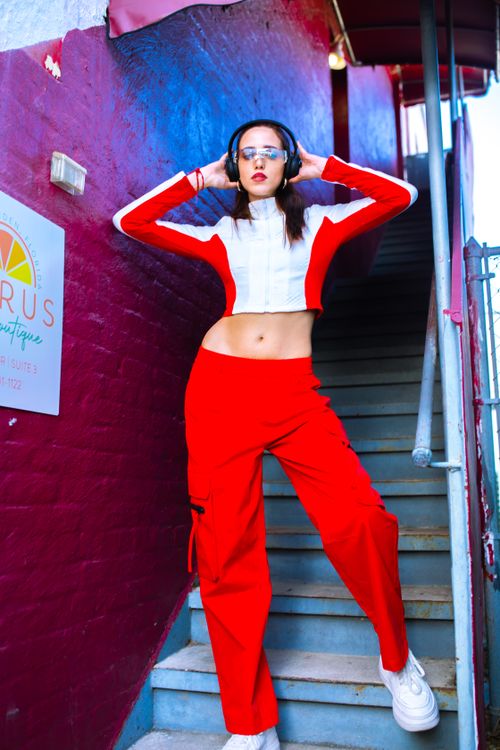Free Stylish woman in red outfit posing with headphones by urban staircase, showcasing fashion and attitude. Stock Photo