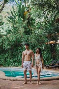 Young couple enjoying a leisurely day by a tropical pool, surrounded by lush greenery.