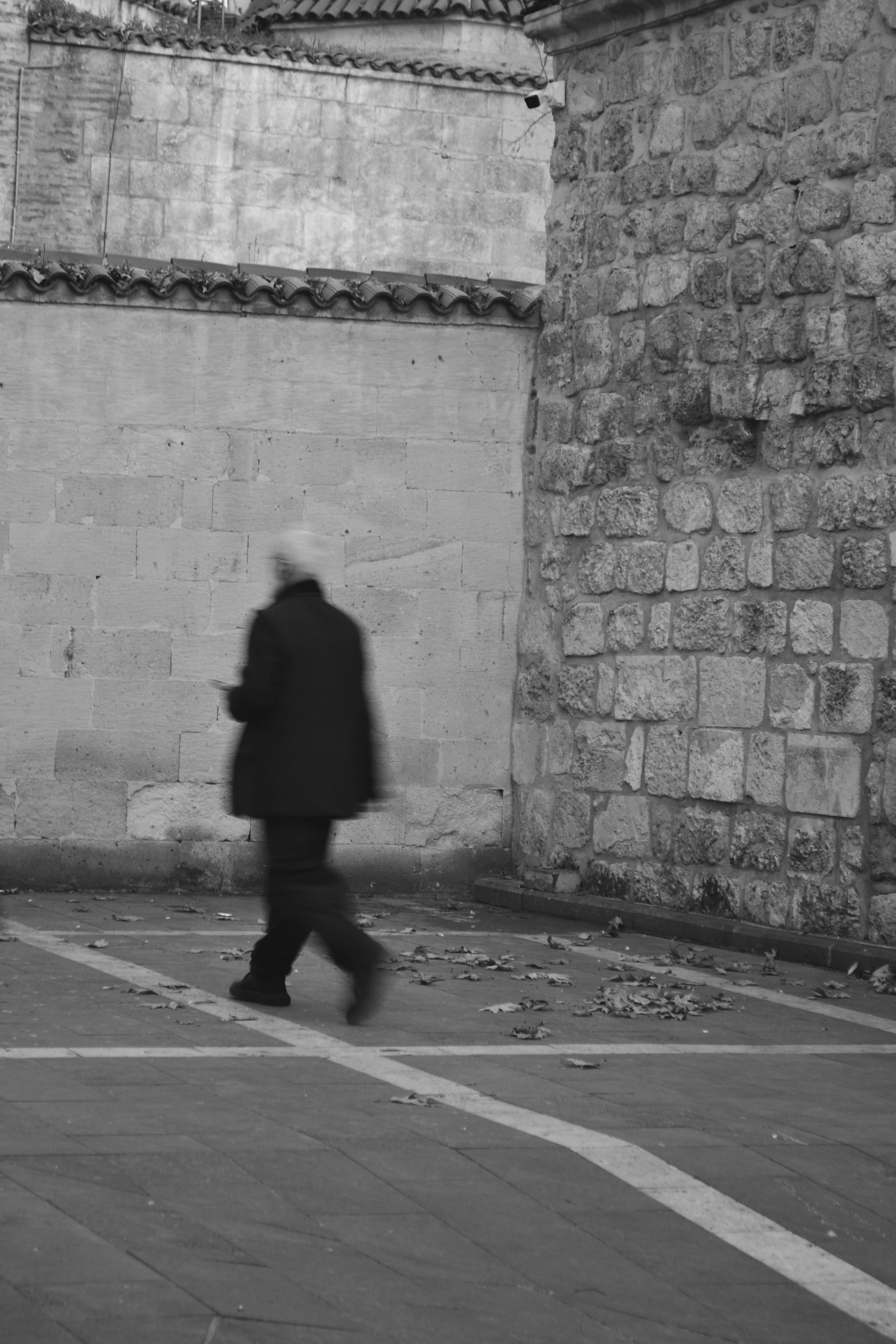 A person walks by an urban stone wall in this black and white street photograph, capturing an artistic moment.