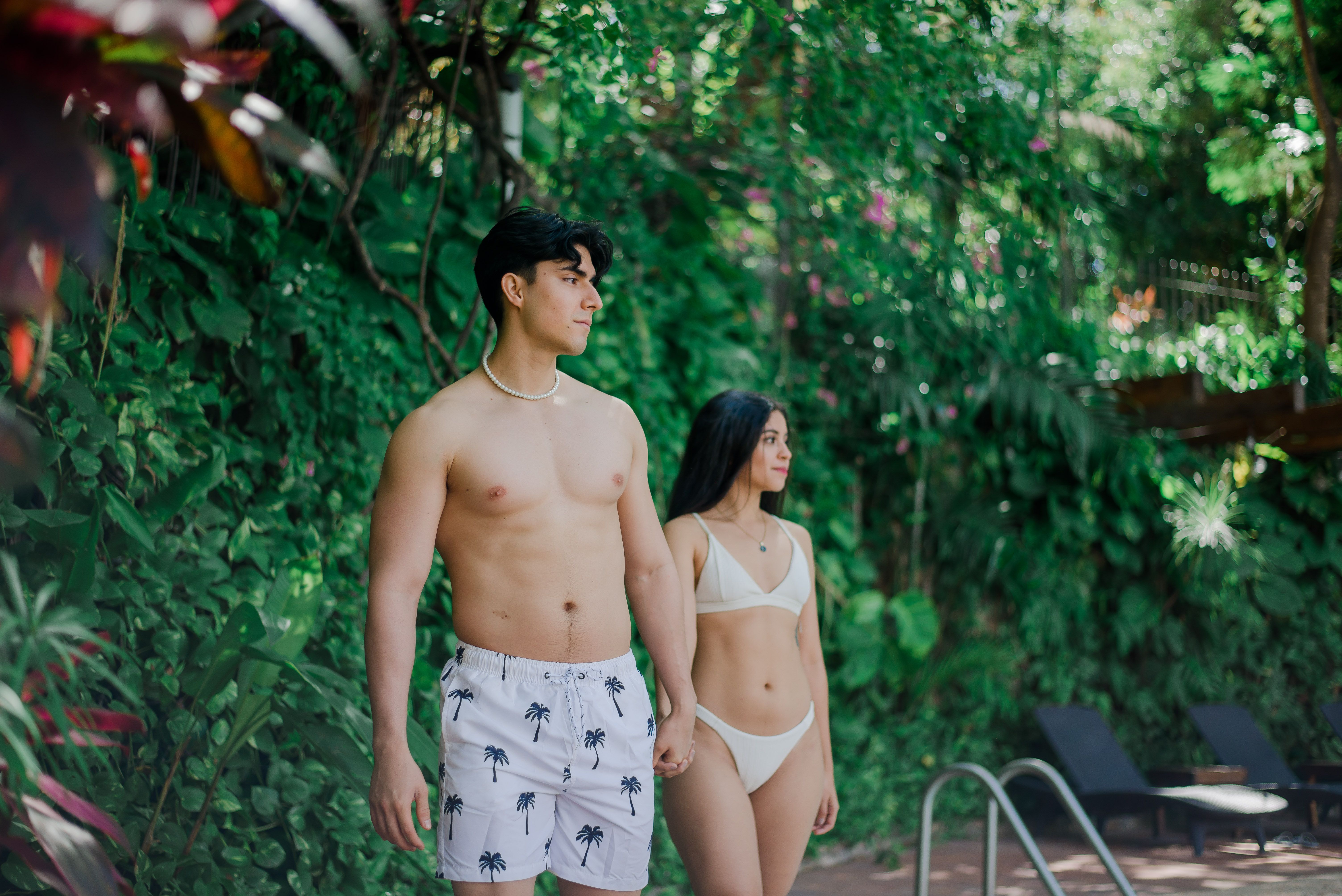 Young couple enjoying a relaxing day by a tropical pool with lush greenery.