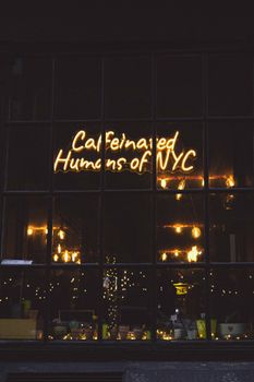 Moody night scene with a neon 'Caffeinated Humans of NYC' sign in a New York cafe window.