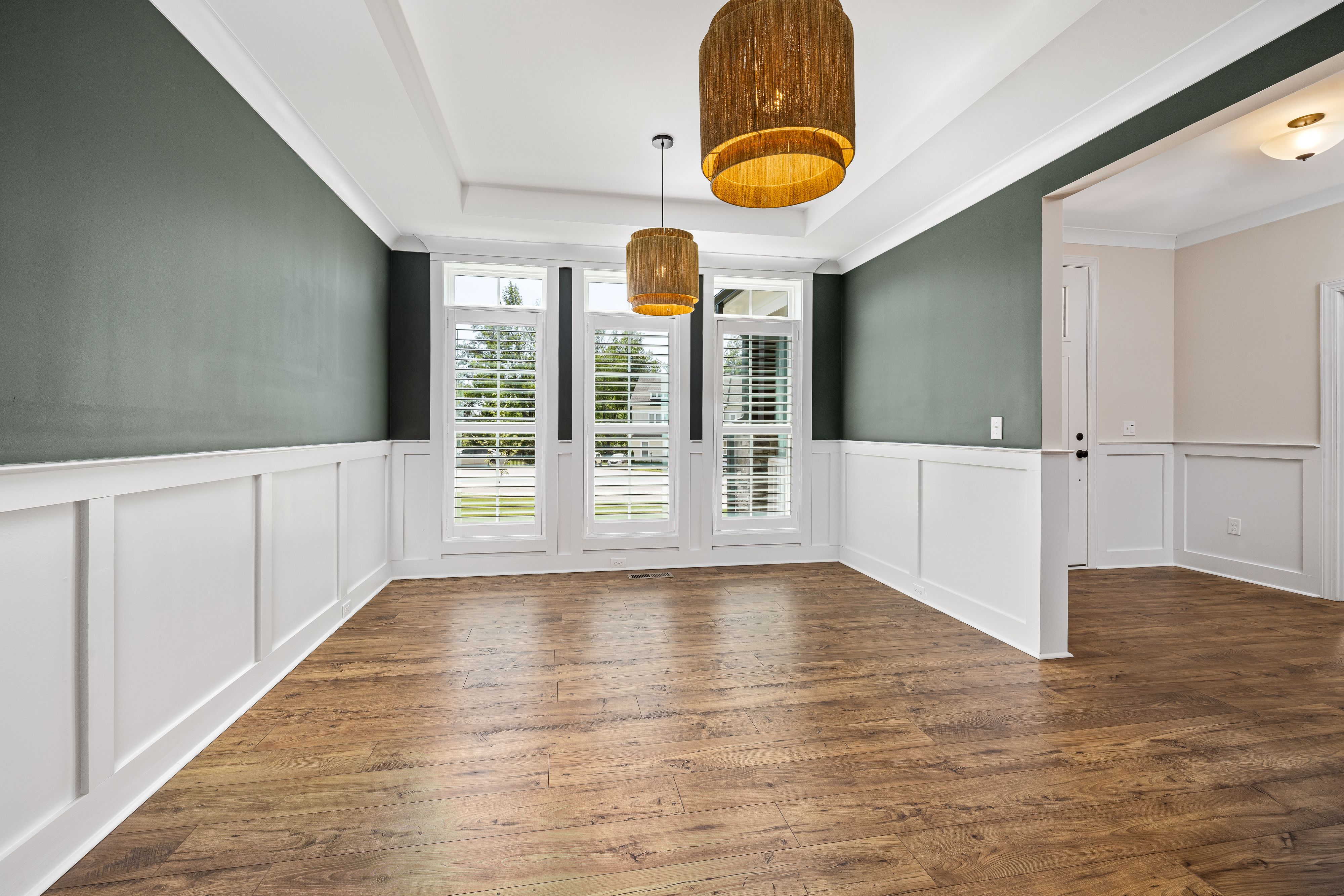 Spacious room with wooden floors, green walls, and large windows, showcasing elegant interior design.