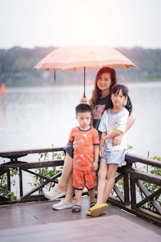 Mother and two children under an umbrella by the lake, enjoying a rainy summer day.