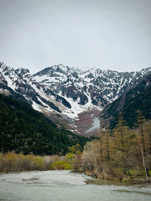 Free Breathtaking view of snow-capped mountains, lush forests, and a serene river in early spring. Stock Photo