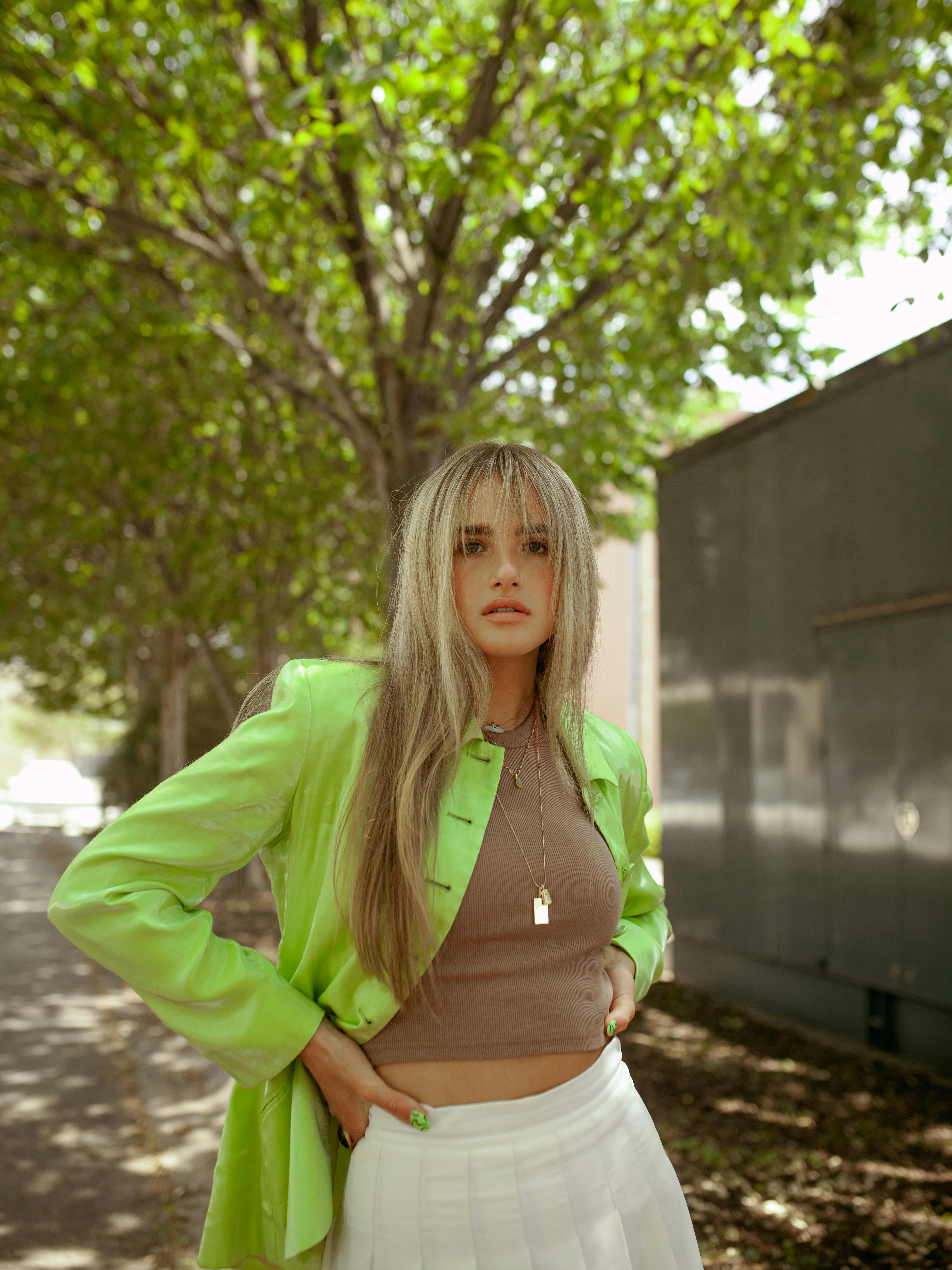 Stylish portrait of a woman in Des Moines wearing a green jacket under leafy trees.