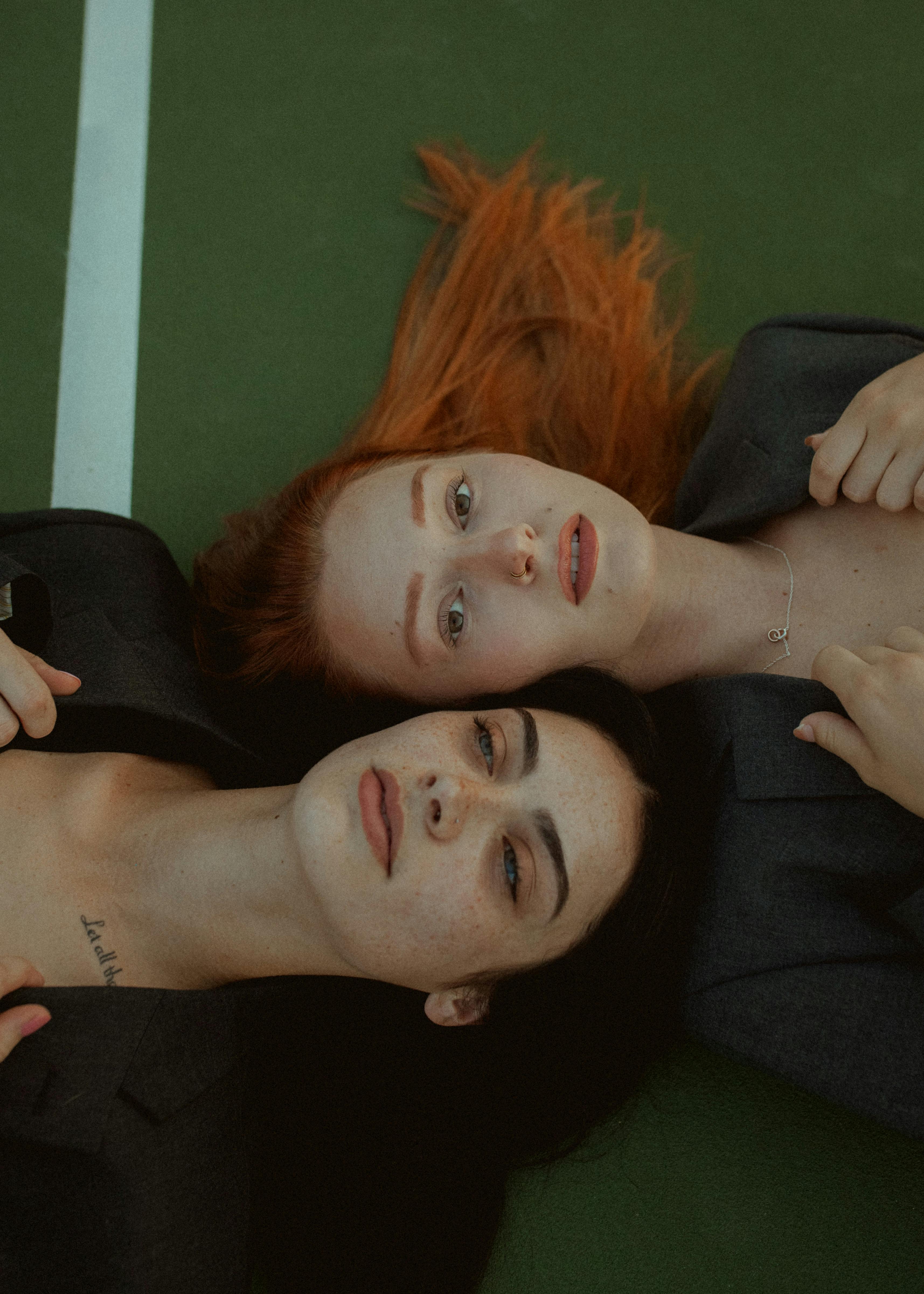 Two women in stylish attire lying on a green surface, showcasing fashion and elegance.