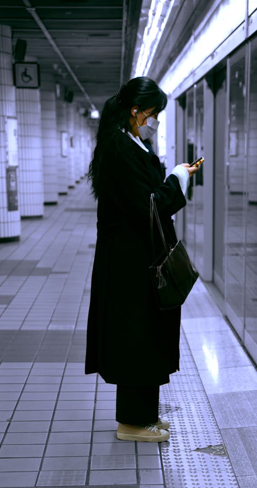 Woman in a Surgical Mask Texting on the Subway Station Platform 