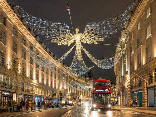 A double decker bus is driving down a street with a large angel hanging from the sky