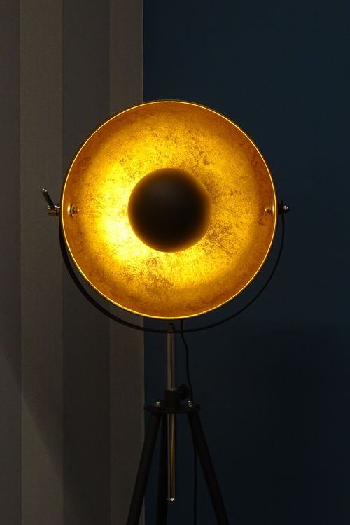 Free A golden retro-style lamp glowing warmly in a modern room with dark walls. Stock Photo