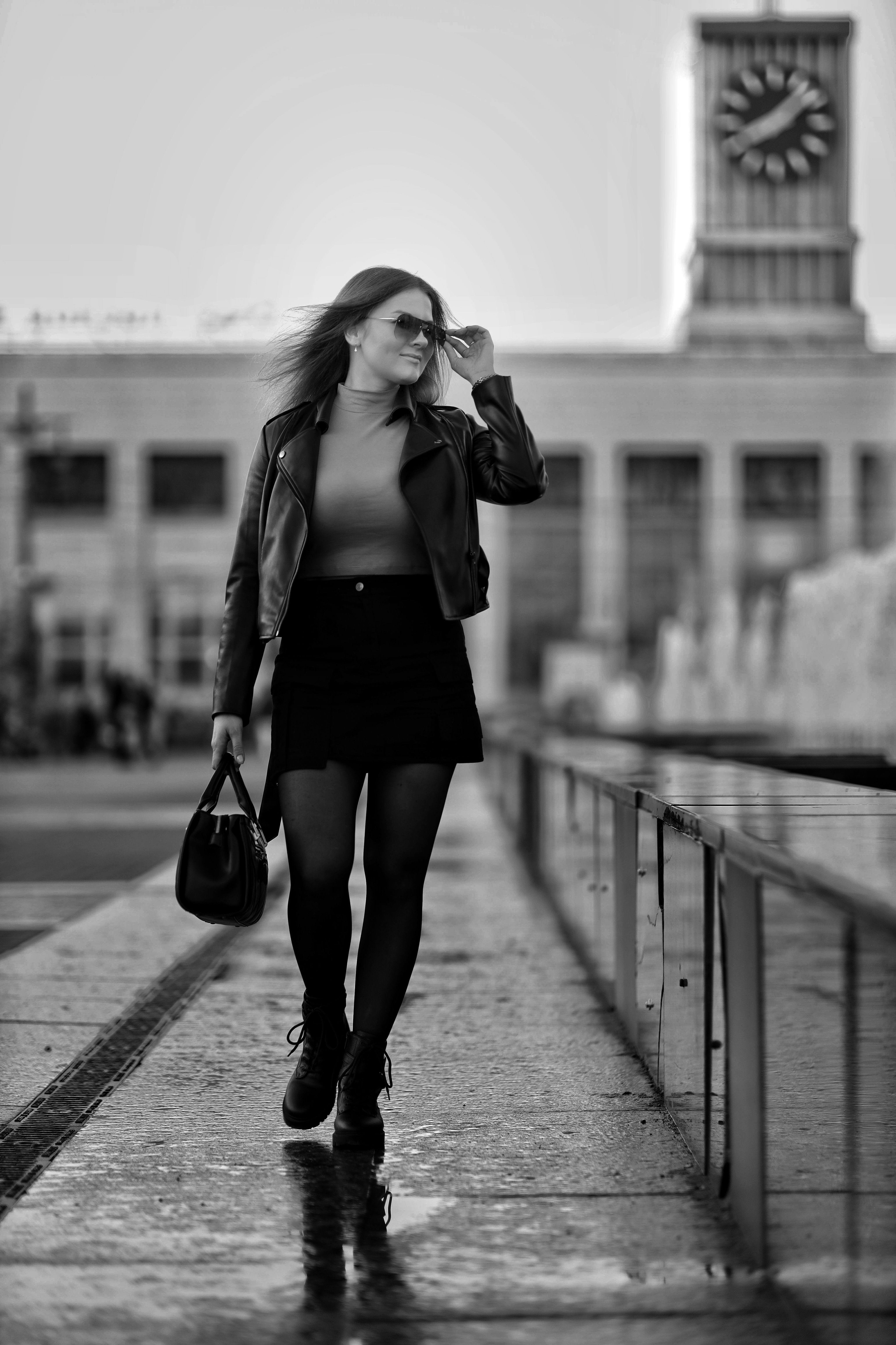 Stylish woman in urban setting wearing a jacket and skirt, walking confidently.