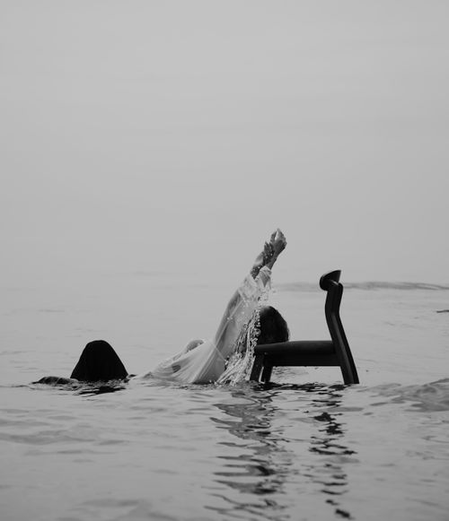 Free A dramatic black and white photo of a woman submerged in water with a chair. Stock Photo