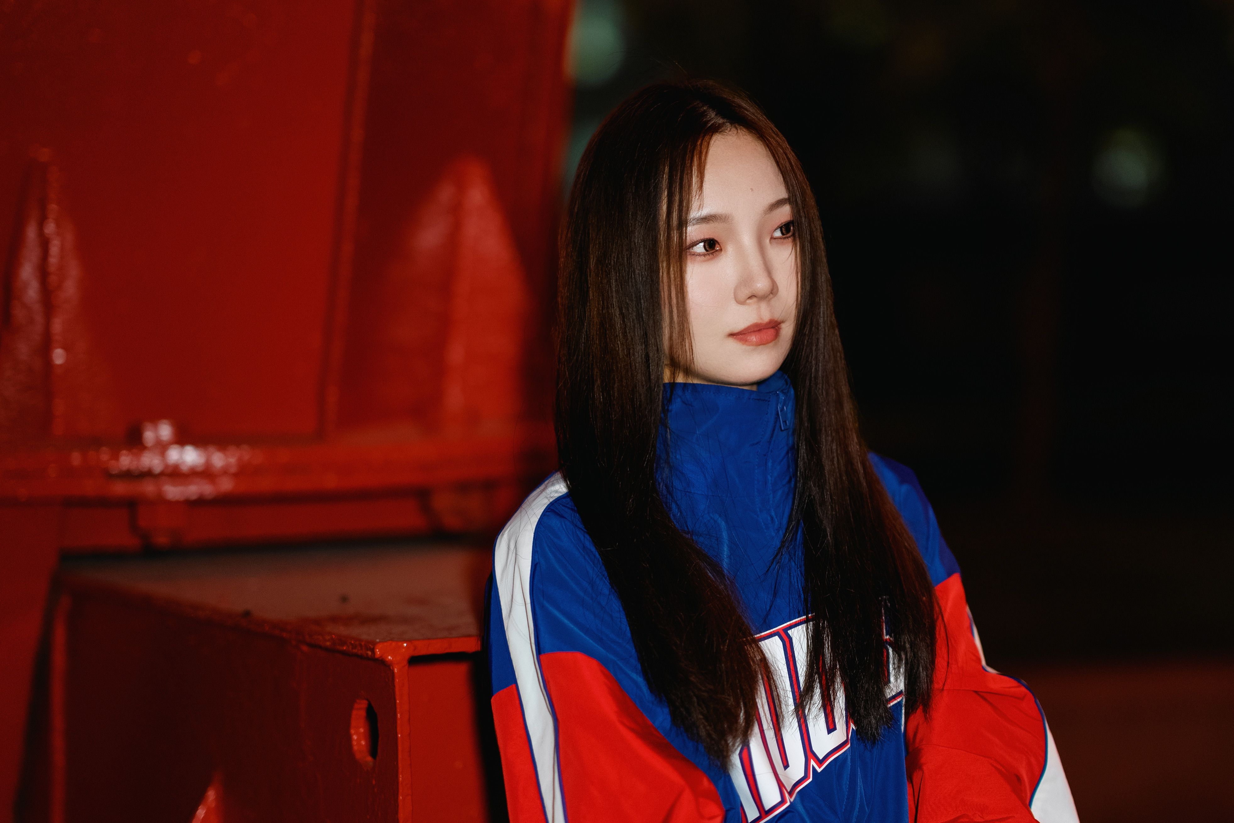 Stylish woman with long hair posing in a colorful sports jacket at night.