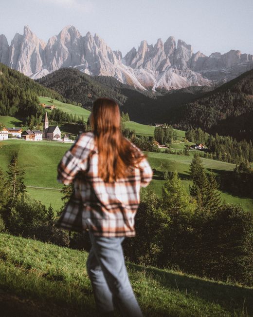 A woman with long brown hair enjoys the scenic view of St. Magdalena's green landscape and mountains in Italy.
