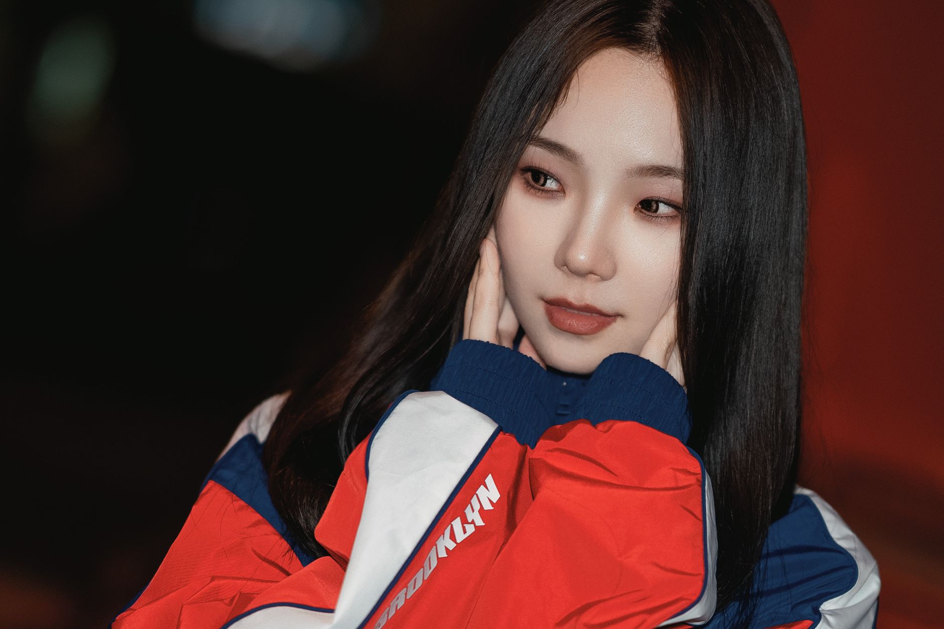 A young woman with long black hair poses thoughtfully with hands on cheeks.
