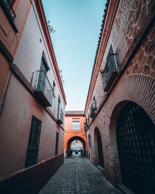 Free Explore a picturesque cobblestone alley in Seville lined with historic buildings and iron balconies. Stock Photo
