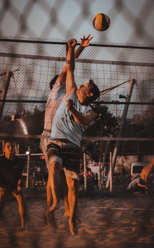 Free Men playing beach volleyball during a dynamic match at dusk, with action and tension in the air. Stock Photo