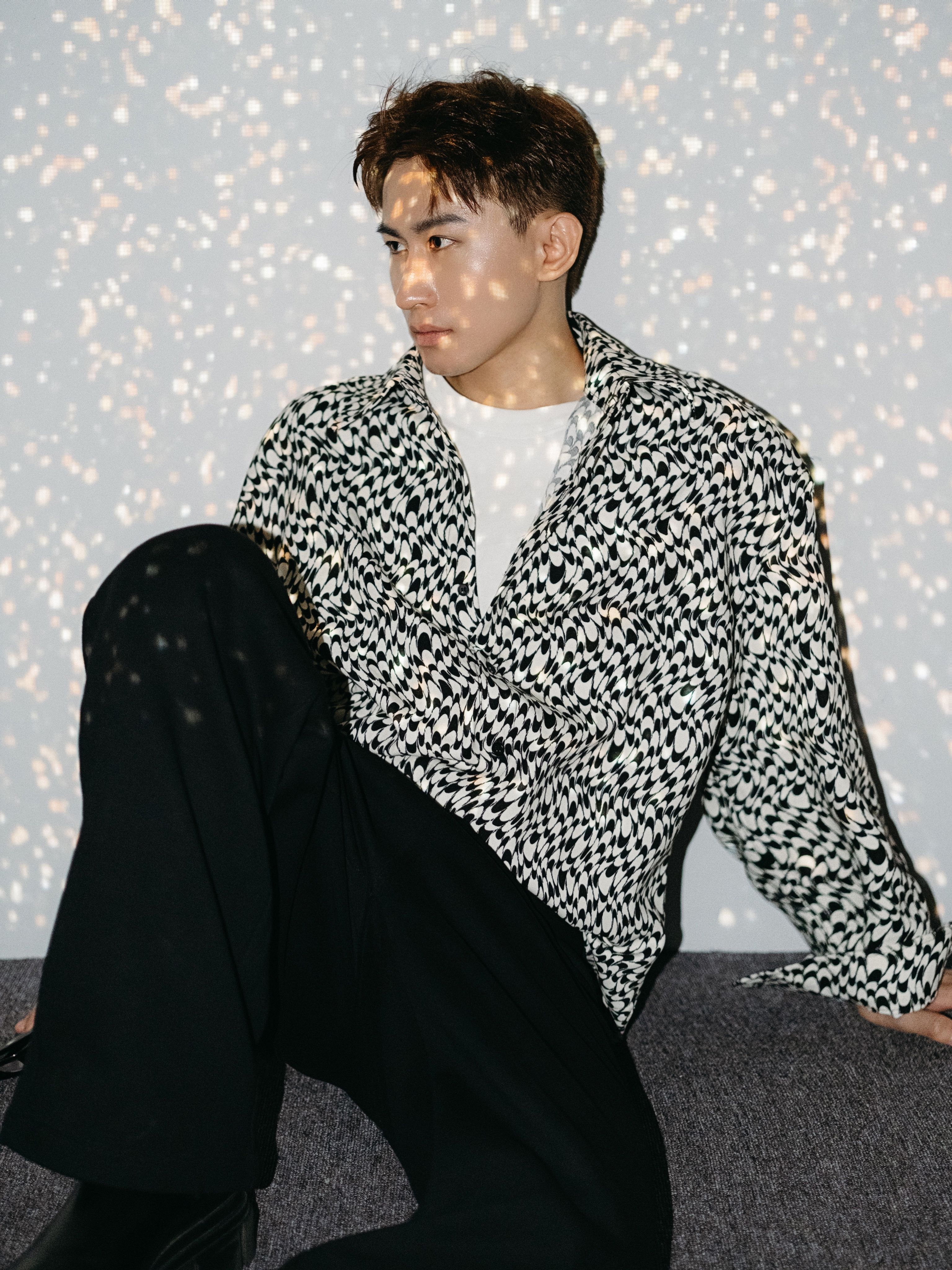 Young man in trendy black and white fashion sitting against a speckled background.