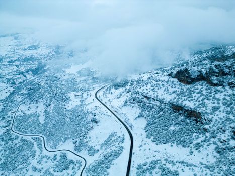 A stunning aerial view showcasing a winding road through snow-covered mountains under a blanket of clouds.