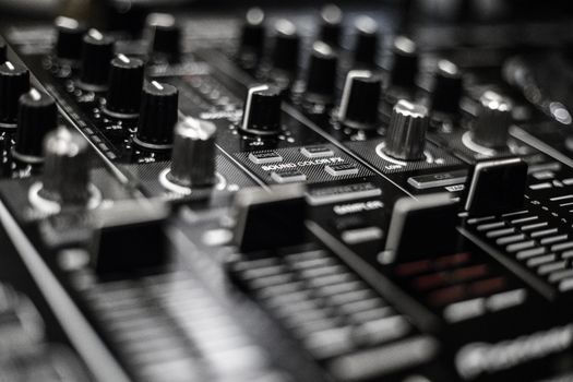 Detailed close-up of a DJ mixer showcasing knobs and sliders in monochrome.