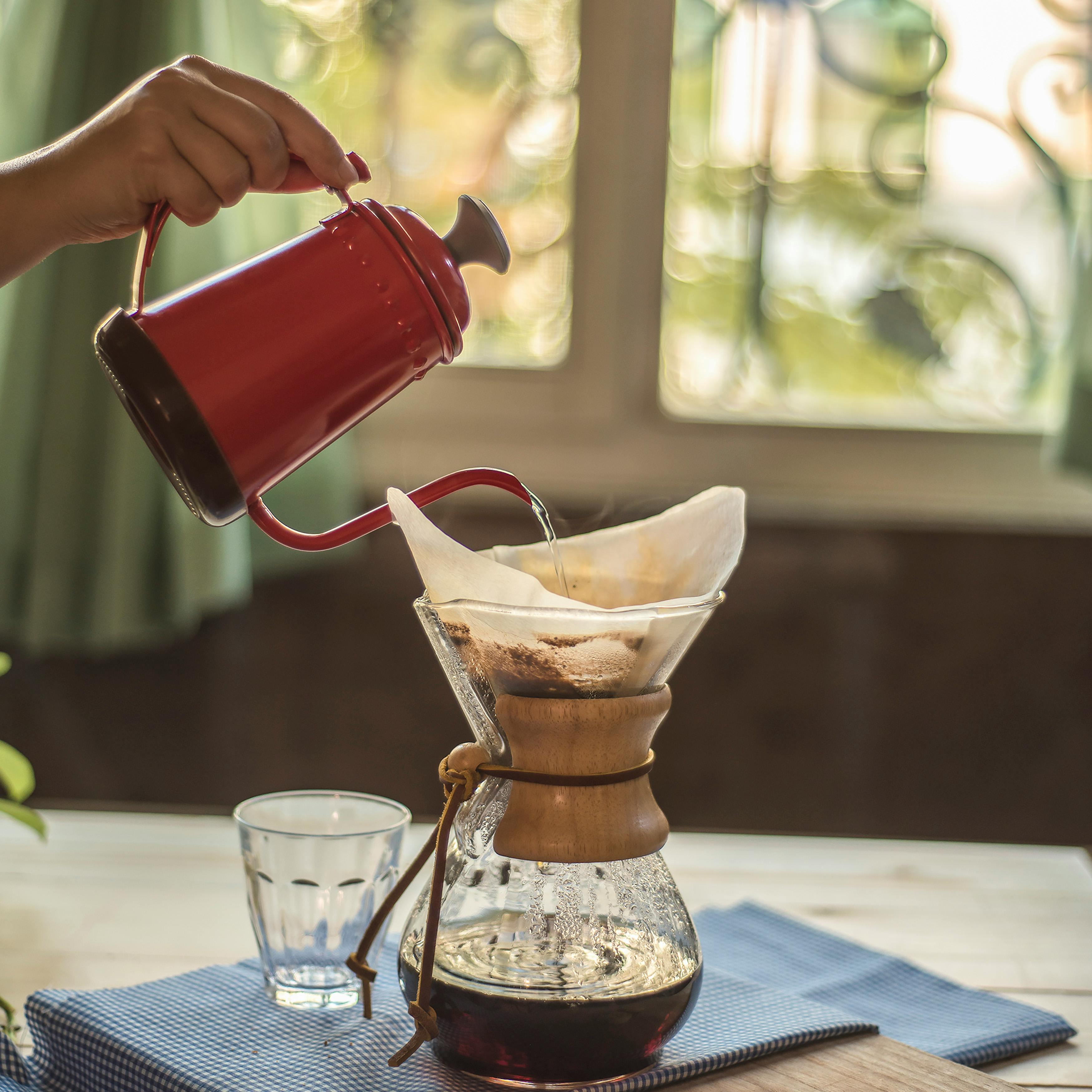 Hand pouring water into a coffee maker from a red kettle. Perfect morning routine.