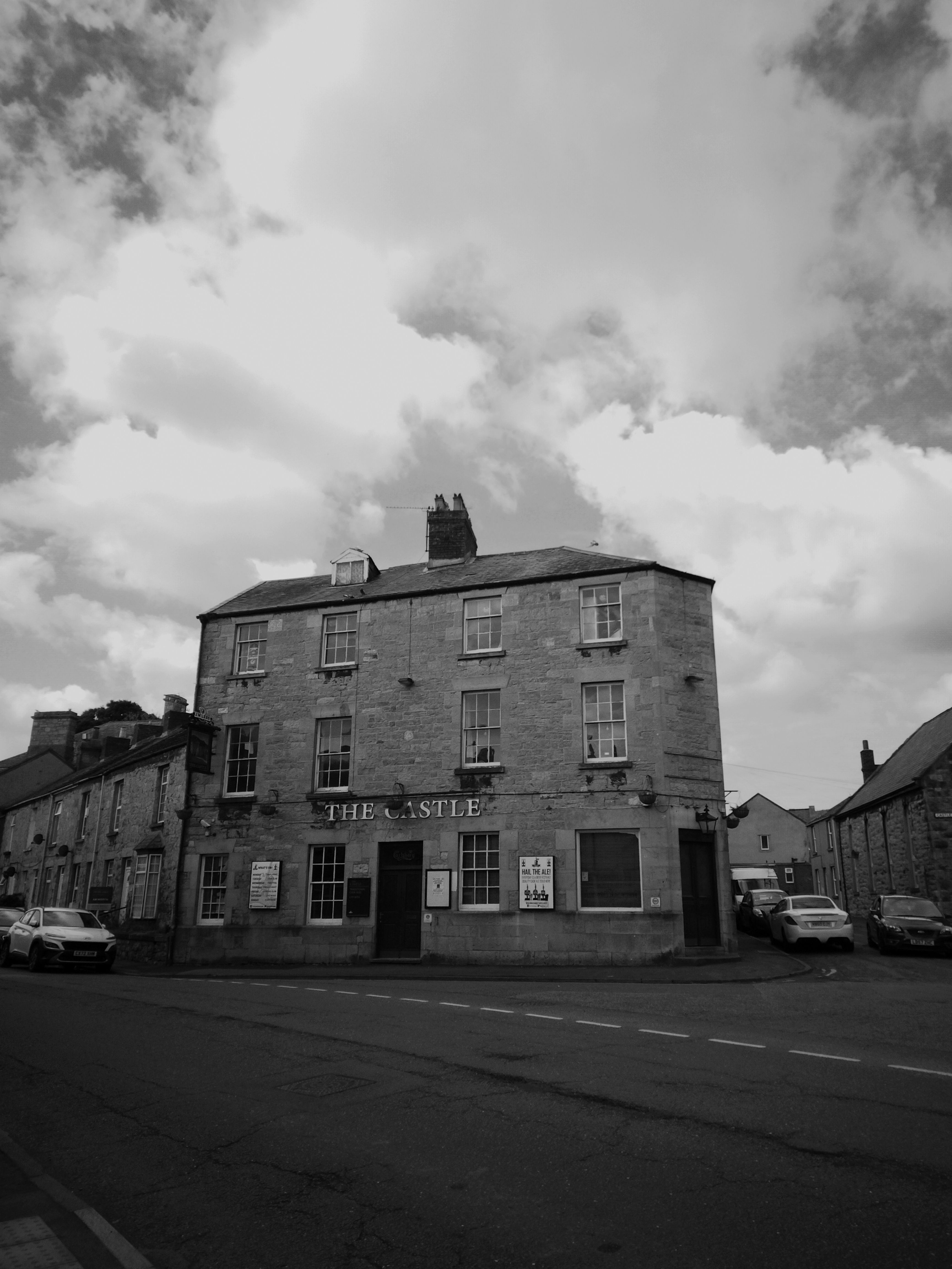 Black and white photo of the historic Castle Hotel on a quiet street in Abergele, Wales, showcasing traditional architecture.