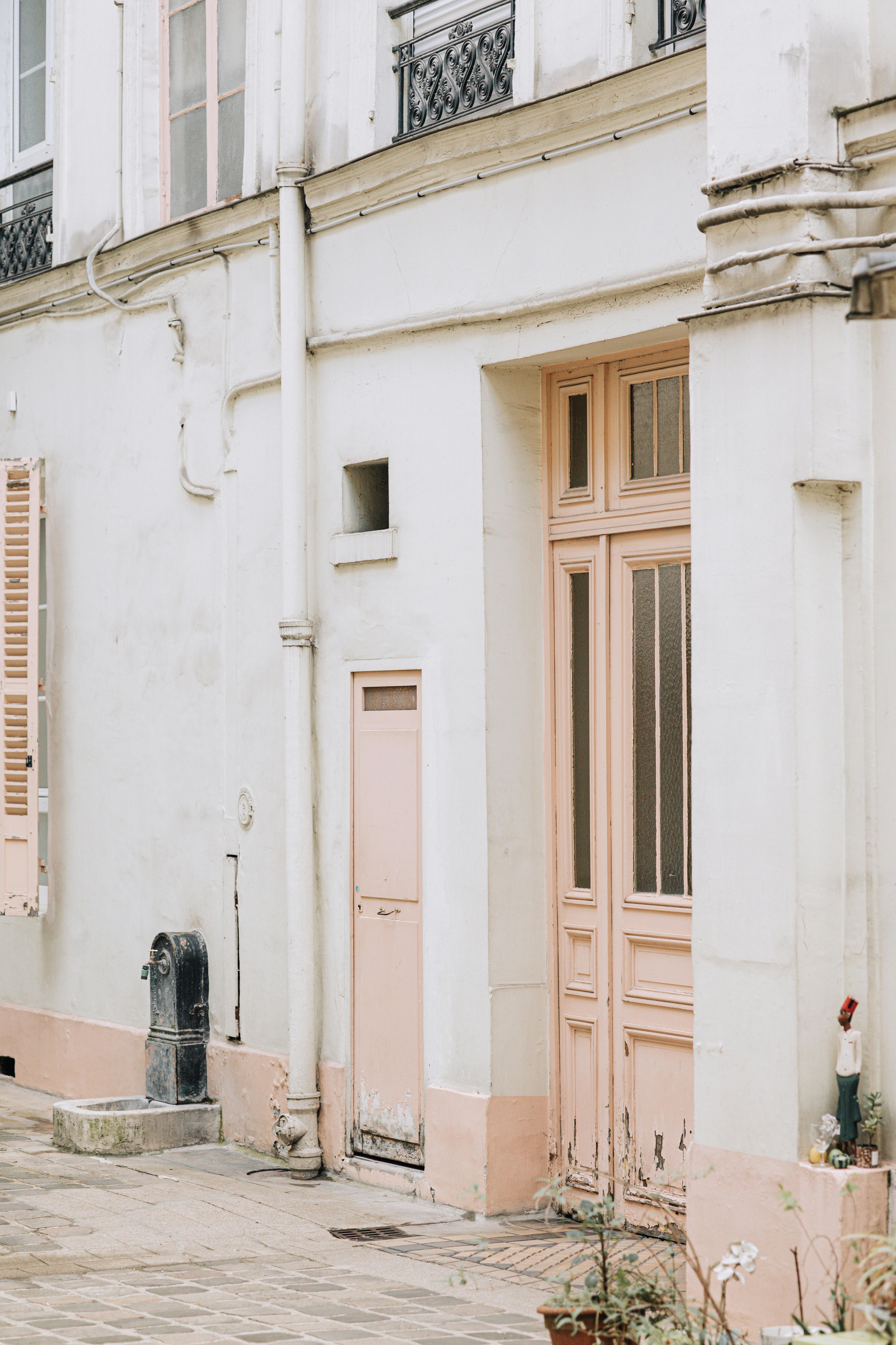 Elegant Parisian building facade featuring pastel pink doors and windows.