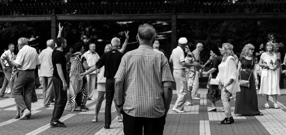 Personas mayores socializando y bailando al aire libre en un animado encuentro urbano capturado en blanco y negro.