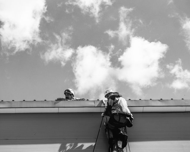 Roofers tracing a roof leak Two roofers in safety gear inspecting a rooftop for leaks