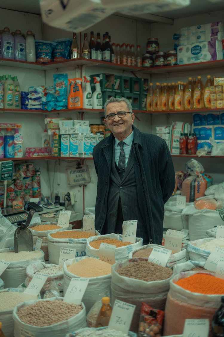 Smiling Man Standing Behind The Counter In His Shop 