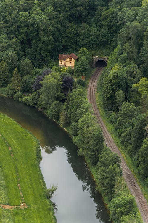 Aerial View of a House between a River and a Railway Tunnel in Mountains Covered with Green Trees