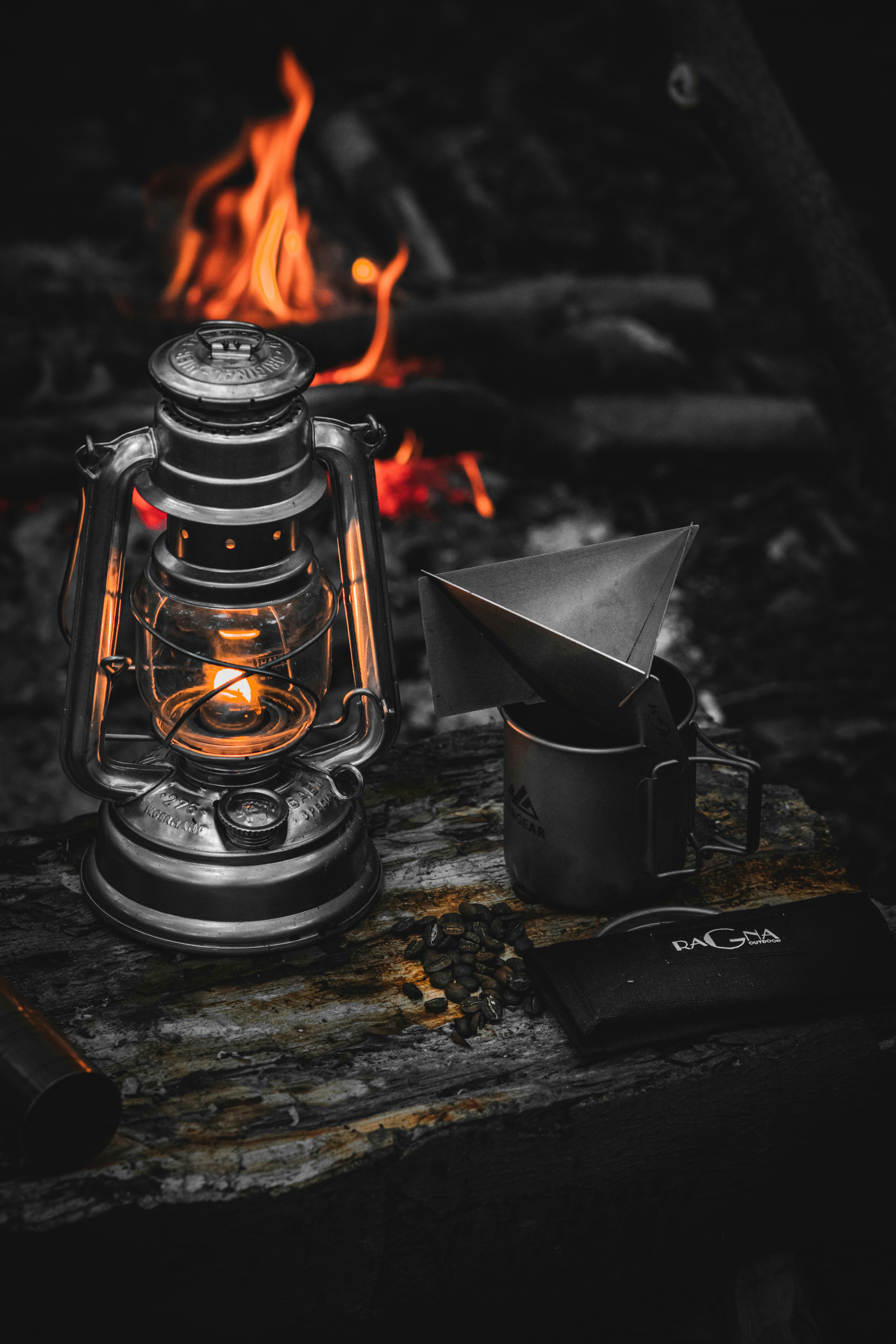 A warm campfire, vintage lantern, and coffee setup create a cozy outdoor atmosphere.