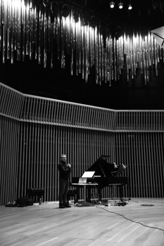 A musican stands by a grand piano on stage in a modern concert hall.