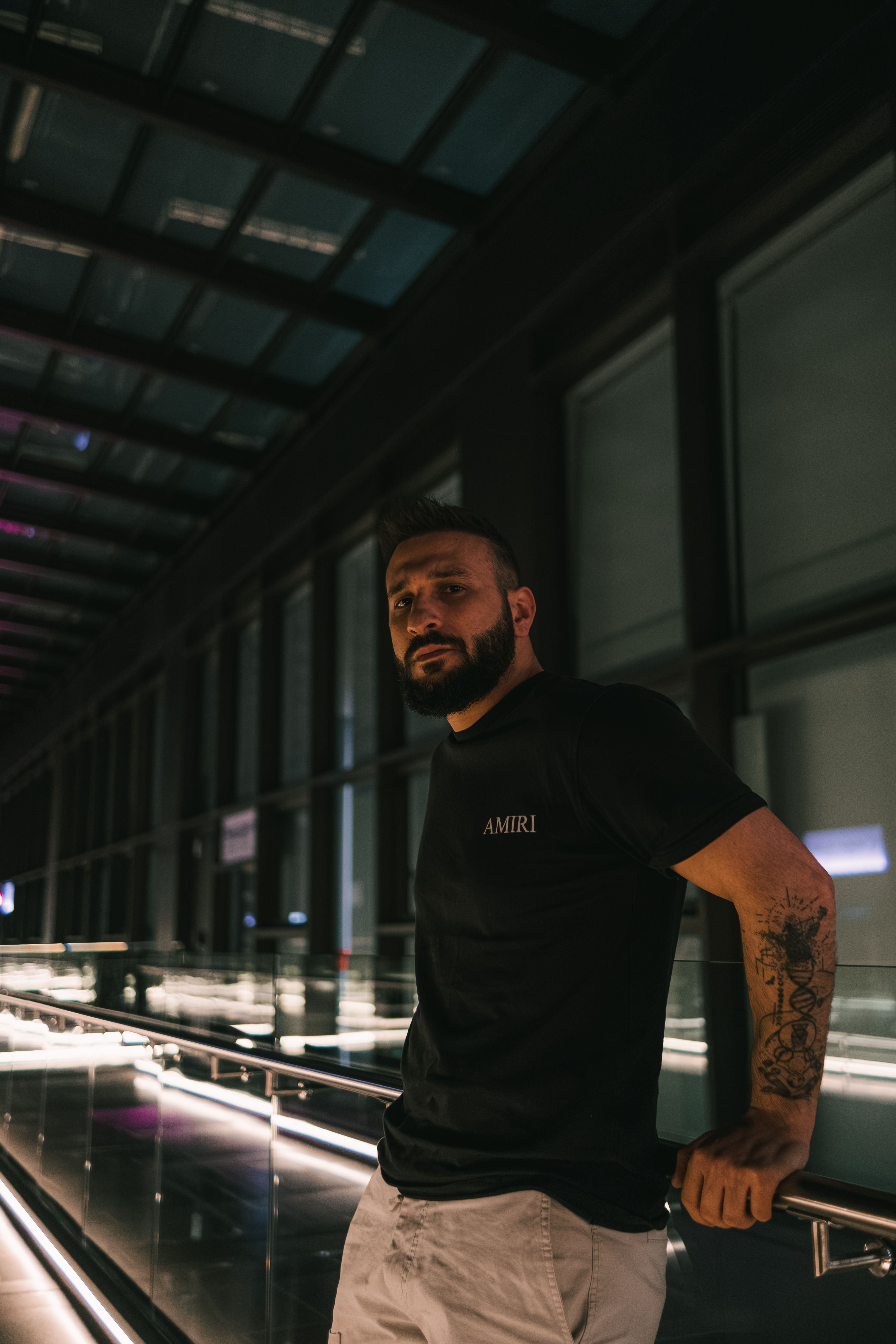Portrait of a bearded man in a modern building, leaning on a metallic railing with soft lighting.