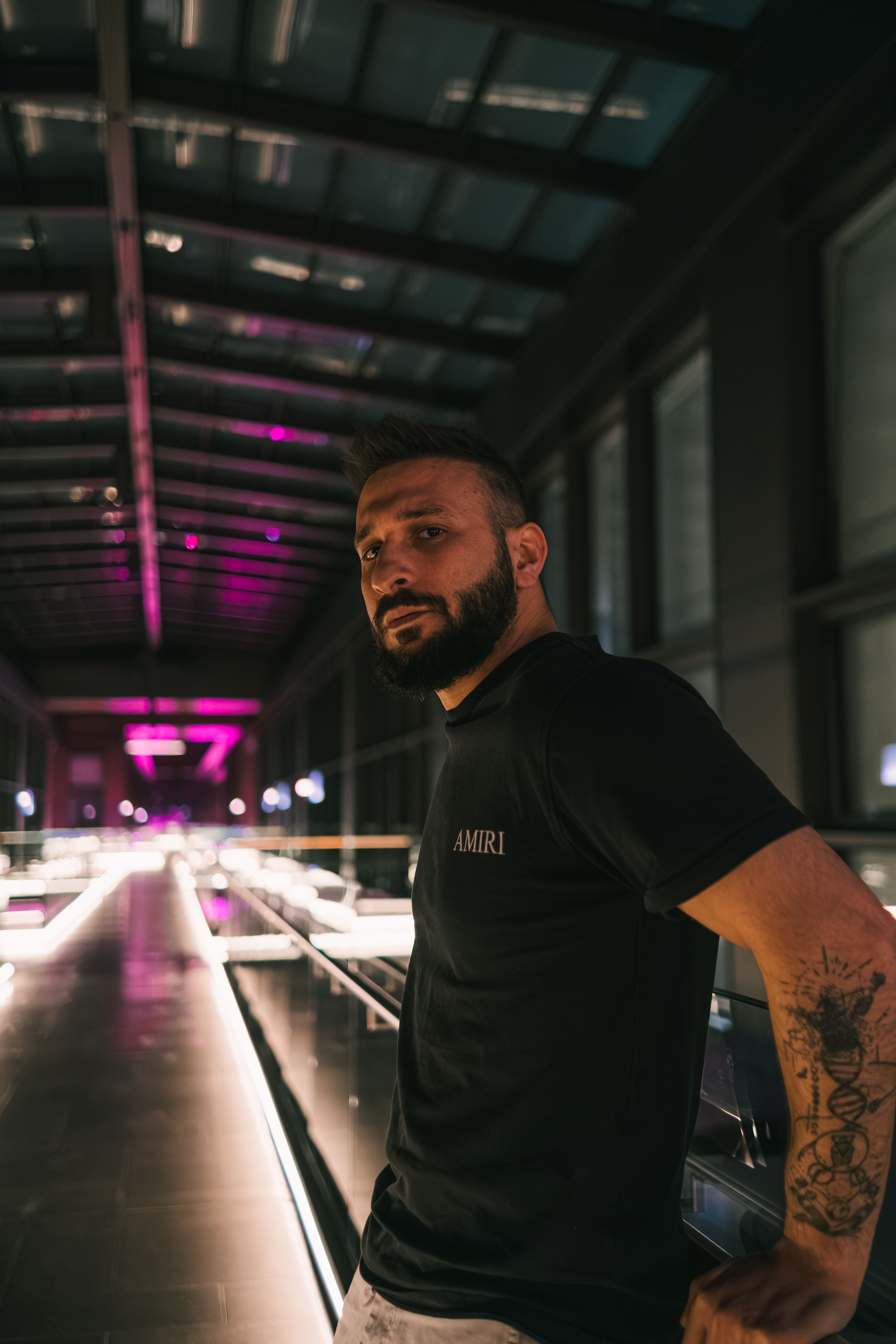 Portrait of a tattooed man standing in an illuminated urban tunnel with contemporary architecture.