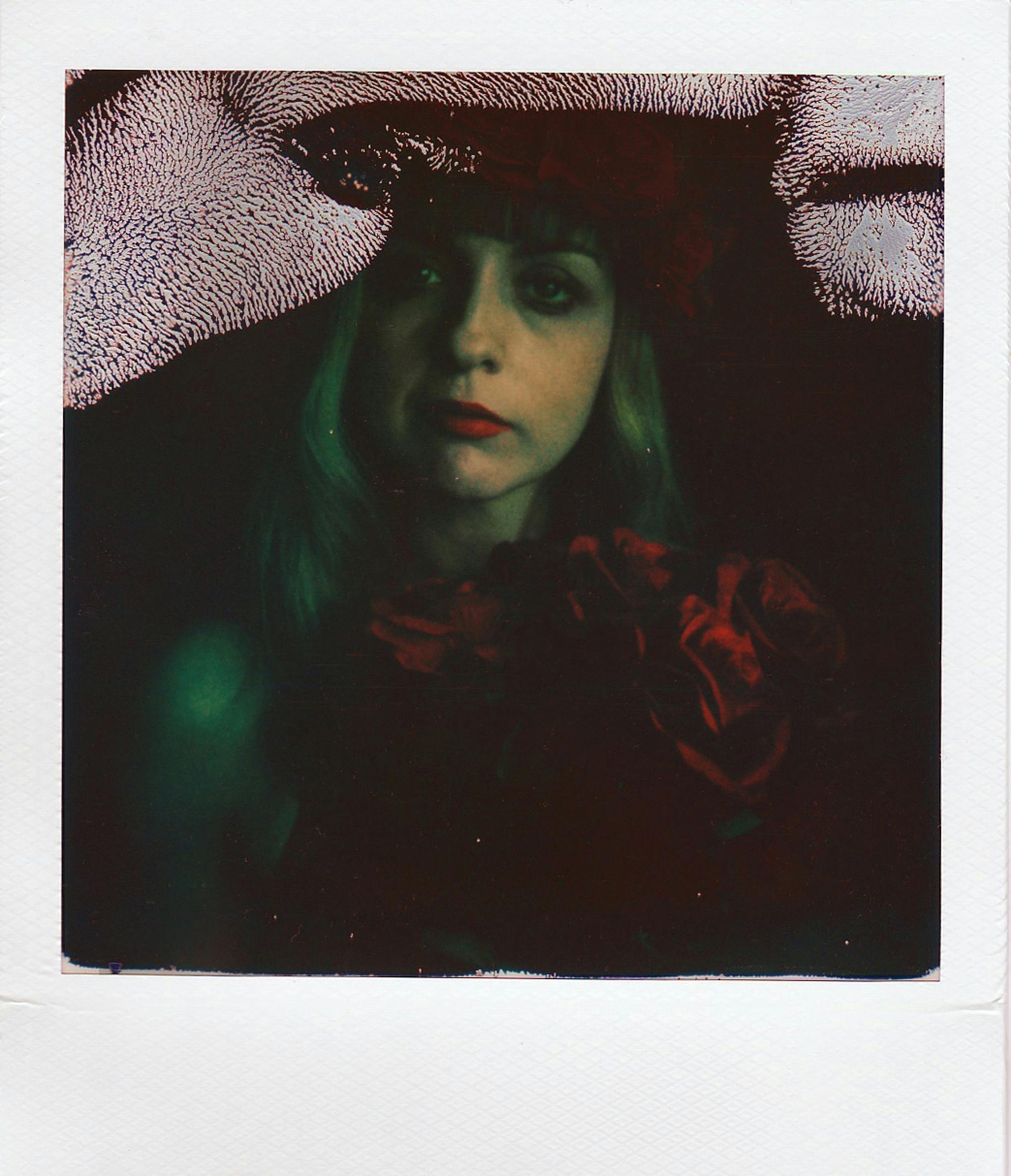 Artistic portrait of a woman in a hat with dark, moody tones in Polaroid style.