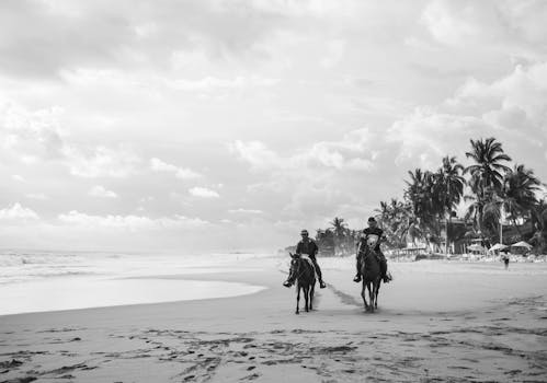Men riding horses on Acapulco beach in black and white, capturing leisure and serenity.