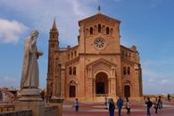 Scenic view of Ta' Pinu Basilica and statue in Gozo, Malta, with visitors exploring the landmark.