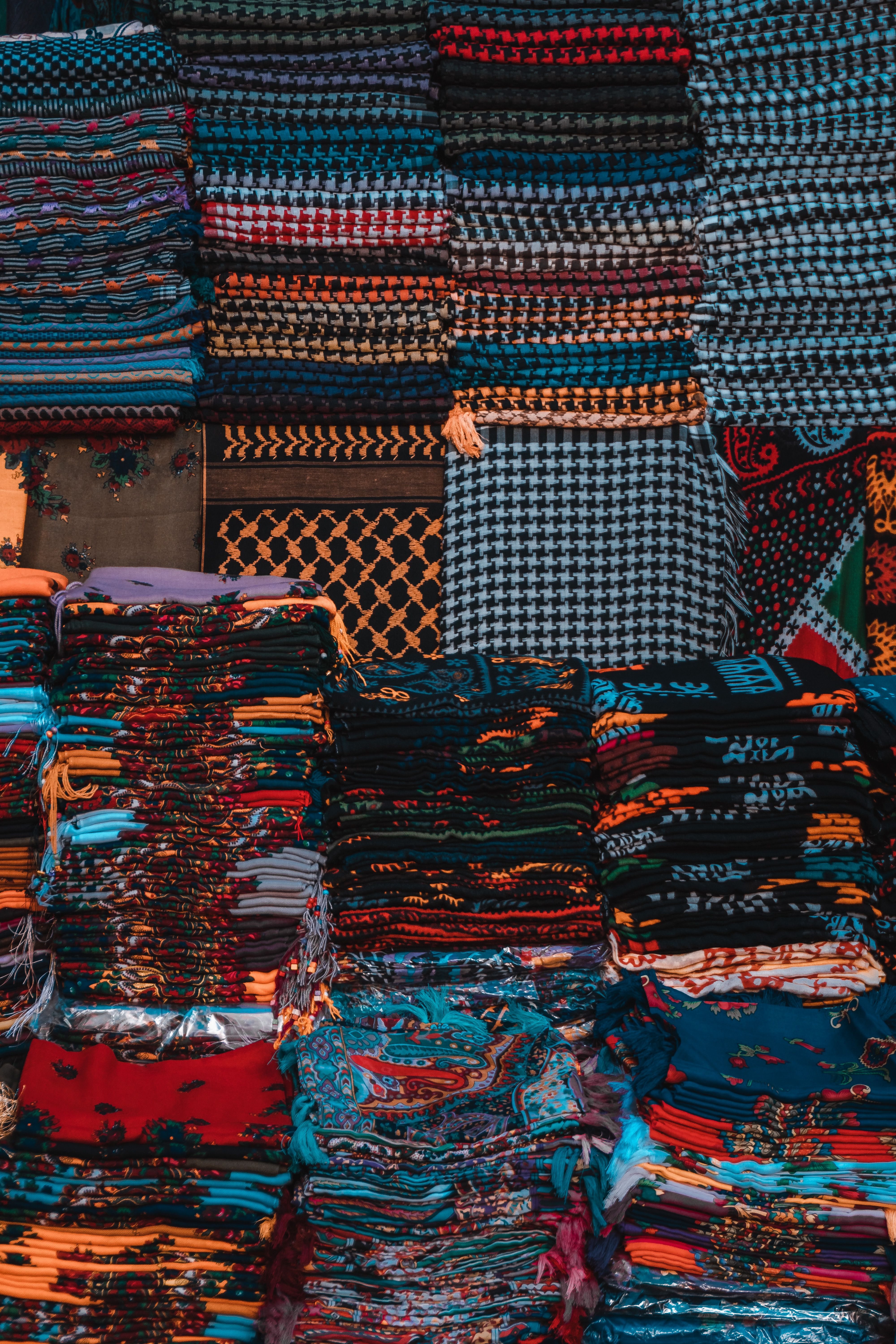 Folded hand-stamped batik sarongs in indigo, rust, and forest green stacked at a traditional Bali textile stall