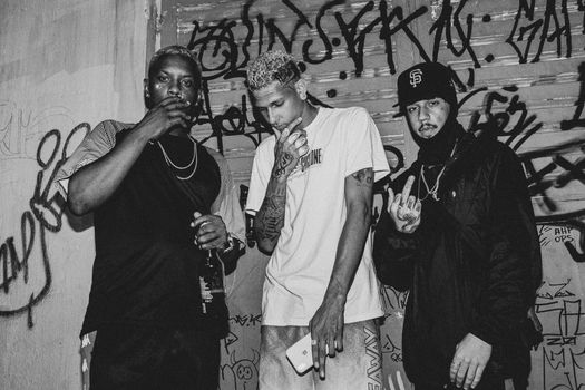 Black and white portrait of three men posing in urban graffiti setting.