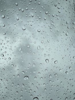 Rain droplets on a glass pane with a blurred background, creating a soothing and moody atmosphere.